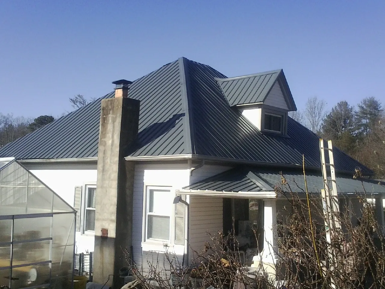 Dark blue standing seam metal roof on a white farmhouse with dormer — Slate & Tile Roof Repair by Roofing Brothers in Westhampton Beach