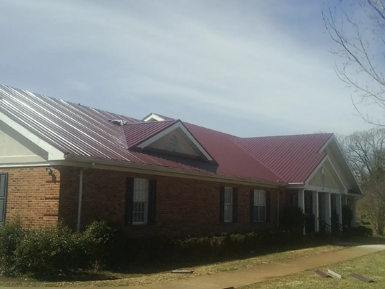 Red metal roof with gabled entries on a long brick building, from a Hail Damage Roof Repair job in Westhampton Beach