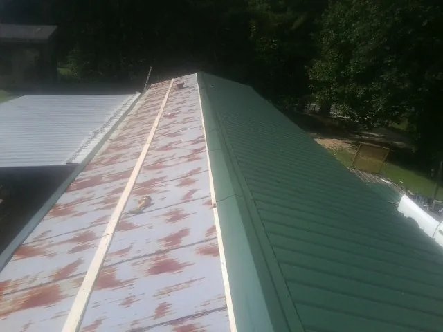 Old rusted panels beside newly installed green metal roofing — Wind Damage Roof Repair by Roofing Brothers in Westhampton Beach
