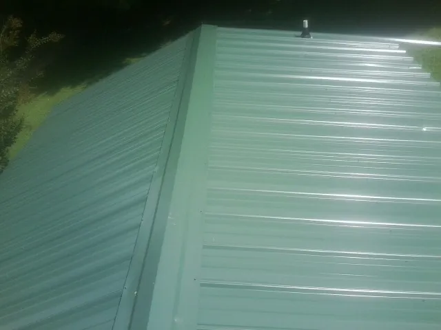 New green metal panels meeting at the ridge of a roof — Flat Roof Repair work by our crew in Westhampton Beach