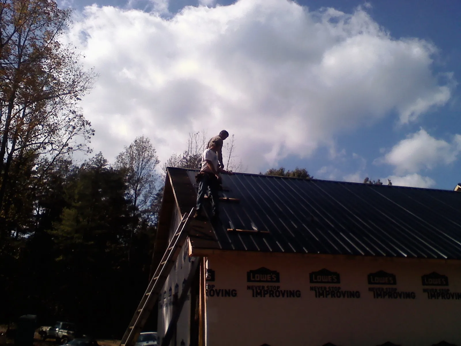 Roofer fastening dark metal panels high against a cloudy sky, from a Roof Inspection job in Westhampton Beach
