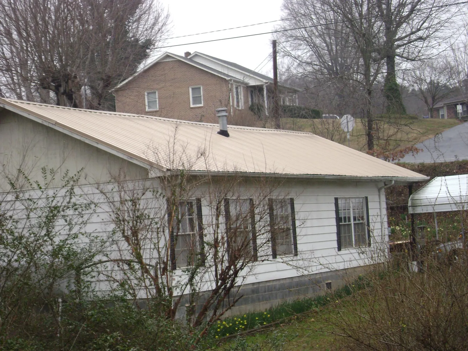 Tan metal roof on a white sided house set into a hillside — Commercial Roofing by Roofing Brothers in Westhampton Beach